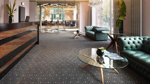 Una hall moderna con tappeto decorato, un tavolino in vetro, un divano verde e un lampadario.