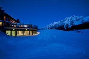 Un edificio moderno con fachada de vidrio, un espacio exterior cubierto y una montaña nevada al fondo.