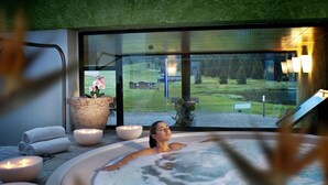 Una mujer relajándose en un jacuzzi con vistas a un paisaje verde y un lago.