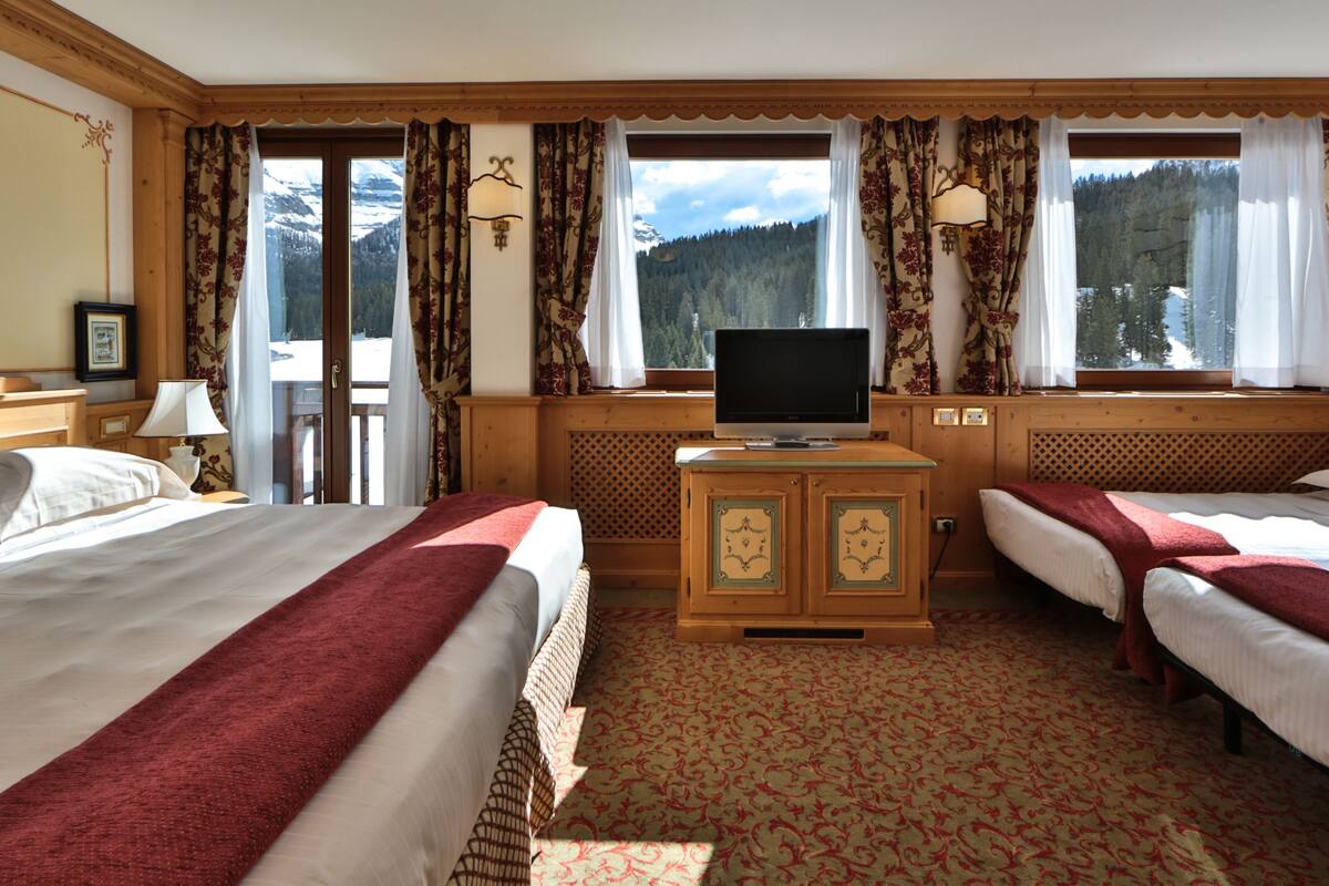 A hotel room with two beds, a television, and a view of mountains through large windows.