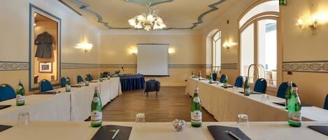 Un salón de conferencias con largas mesas, sillas y una pantalla para proyector.