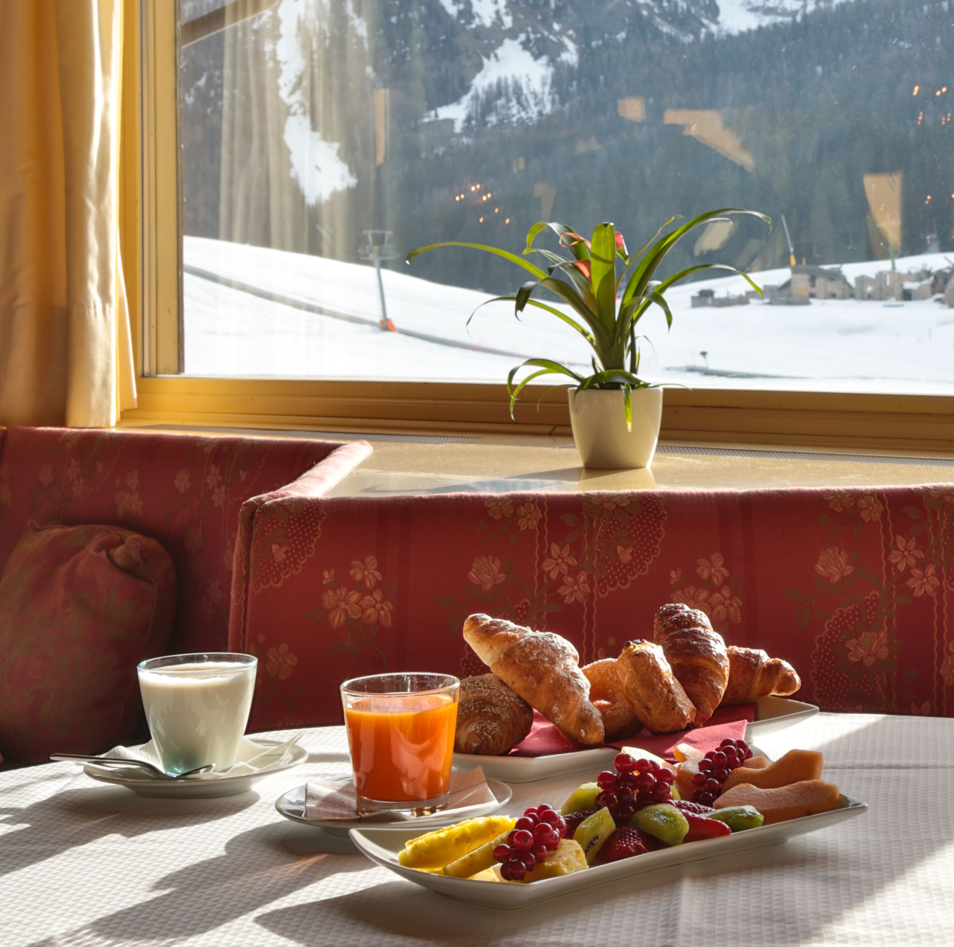 Une table dressée pour le petit-déjeuner, avec des viennoiseries, des fruits et des boissons, placée près d’une fenêtre offrant une vue sur un paysage enneigé.