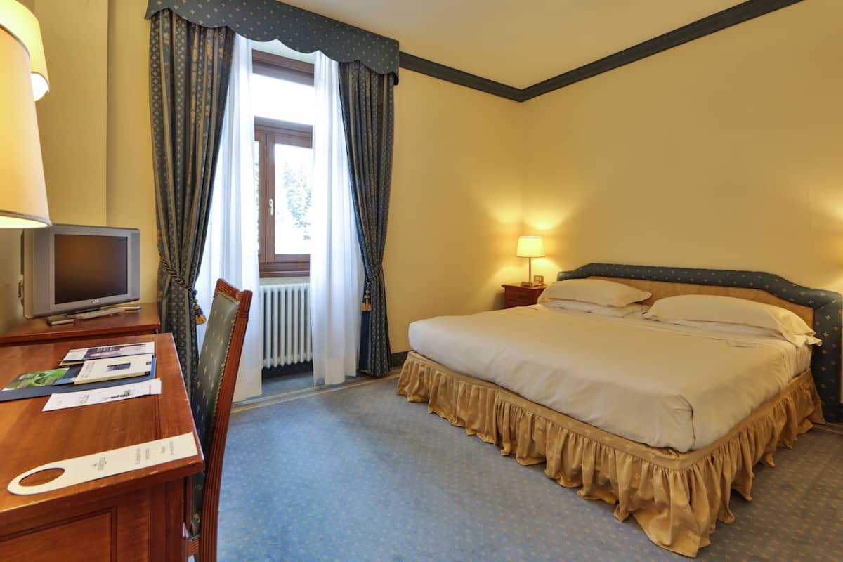 Una habitación de hotel con cama, escritorio con televisor y una silla.