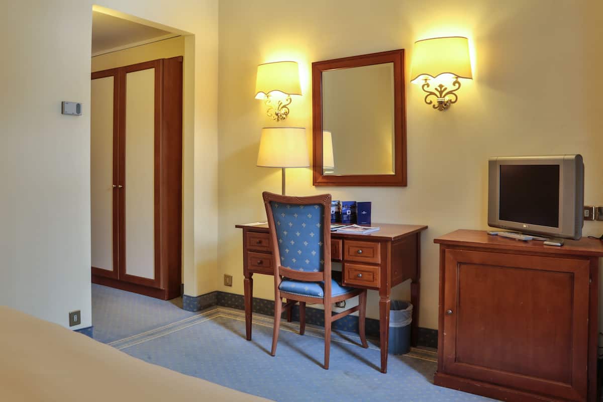 Una habitación de hotel con un escritorio de madera, una silla, un televisor y dos lámparas fijadas a la pared.