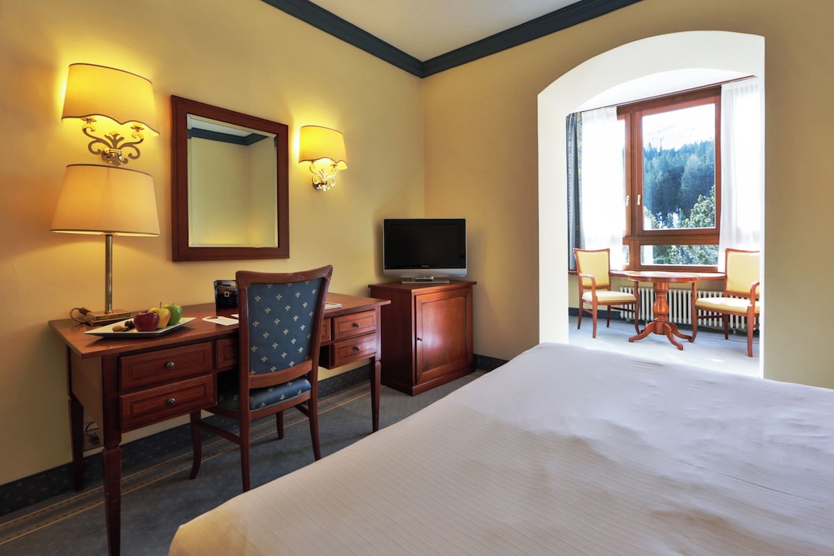 Une chambre d’hôtel comprenant un lit, un bureau, une chaise, une télévision et un balcon avec des chaises.