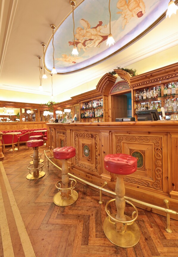 A bar area with wooden bar counters, red cushioned stools, and a decorative ceiling mural.