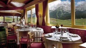Un restaurante con mesas redondas dispuestas para comer, grandes ventanales que ofrecen vistas a las montañas y un techo de madera.