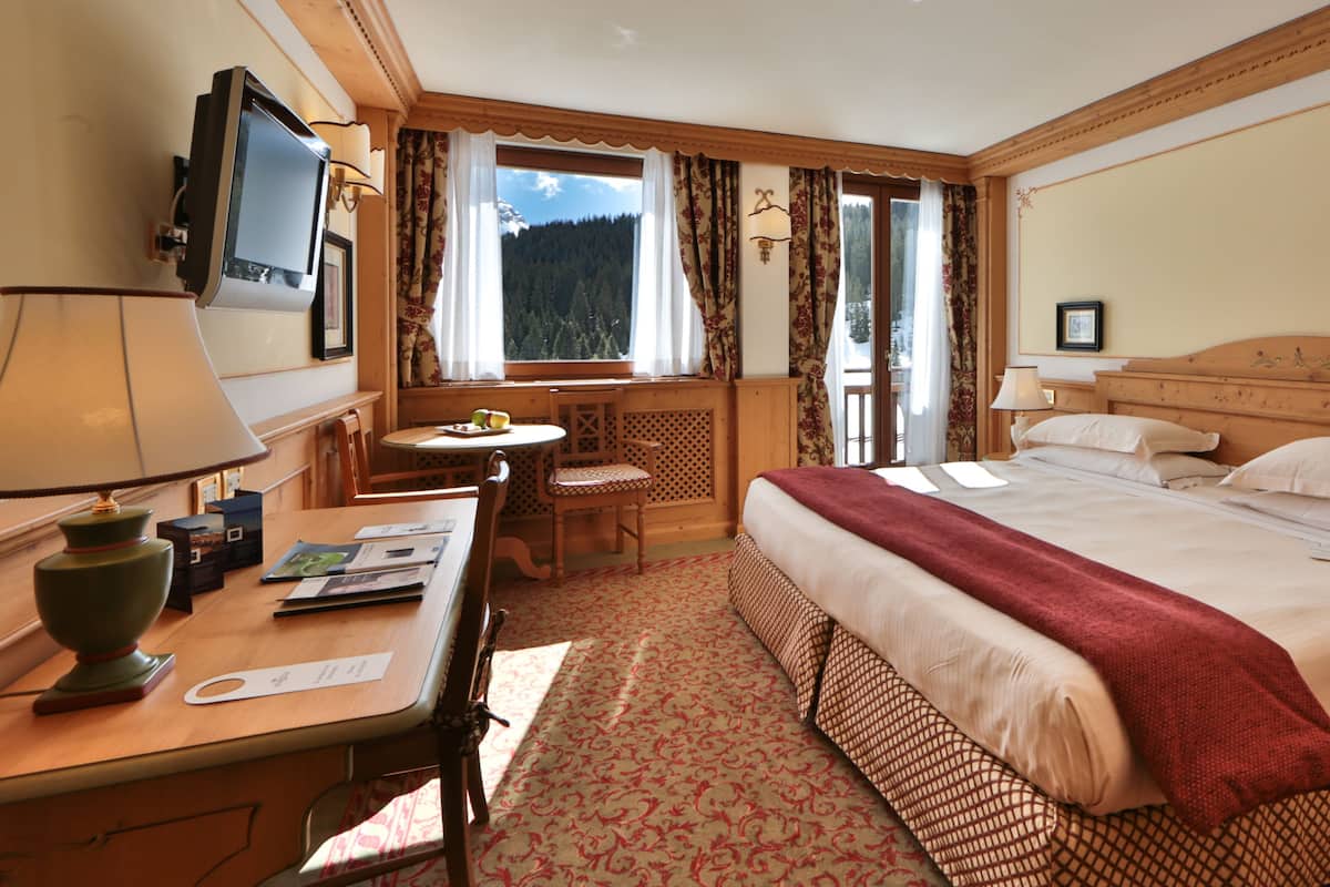 A hotel room with a bed, a desk with a lamp, a chair, a TV, and a window with curtains.