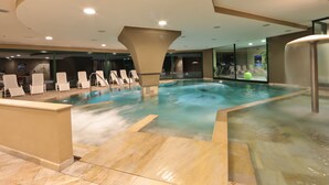Una piscina interior moderna con agua cristalina, sillones de descanso y un muro de vidrio que ofrece vistas al exterior.