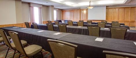 A conference room with long tables, chairs, and a projector screen.