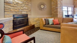 A living room with a stone fireplace, a sofa set, and a patterned rug. - Drury Inn & Suites Amarillo (Amarillo)