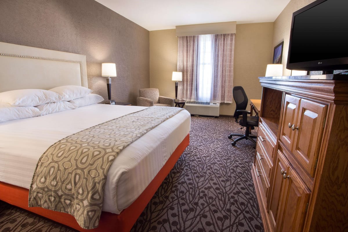 A hotel room with a large bed, a desk, a chair, a television, and a wardrobe.