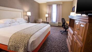 A hotel room with a large bed, a desk, a chair, a television, and a wardrobe.