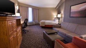 A hotel room with a bed, a sofa, a TV, a desk, and a wardrobe.