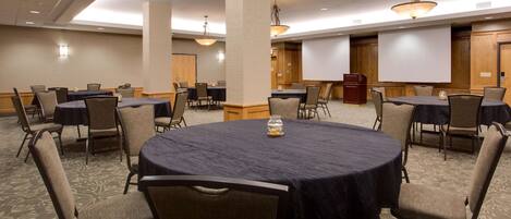 A conference room with round tables, chairs, and a projector screen.