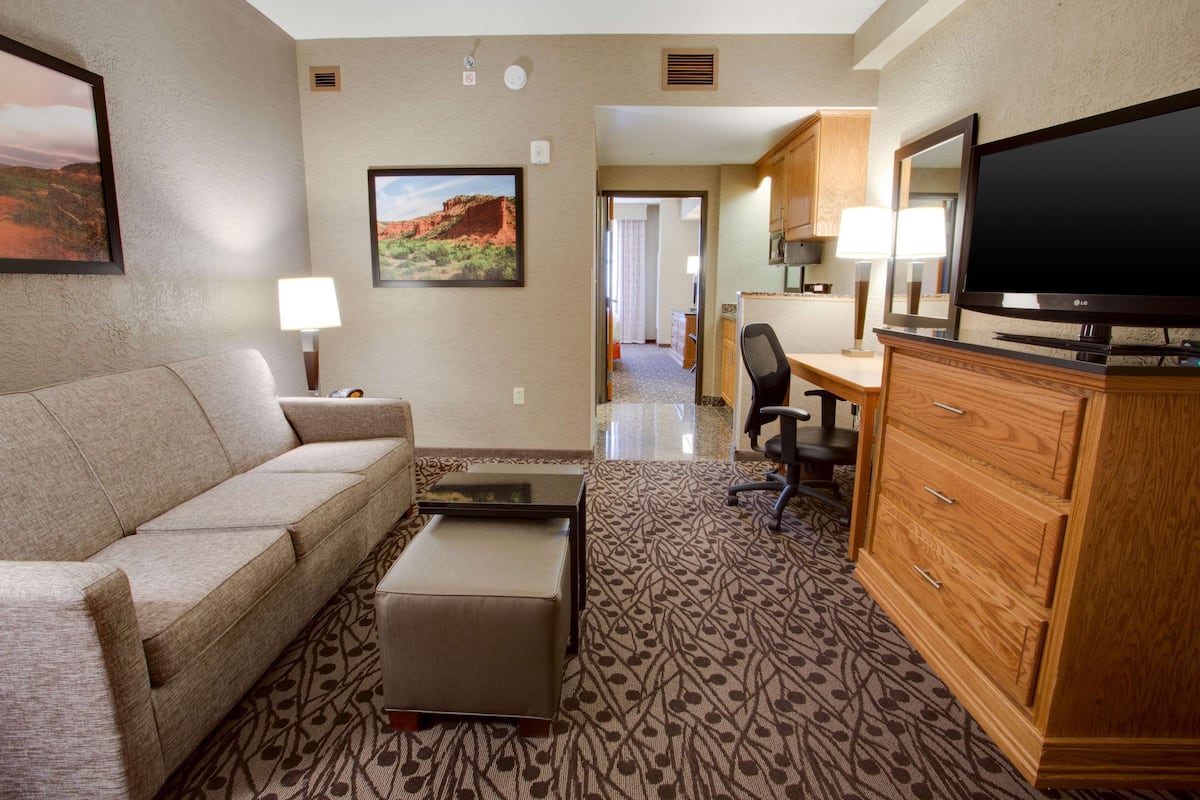 A hotel room with a sofa, a small table, a TV, a wooden cabinet, and a patterned carpet.