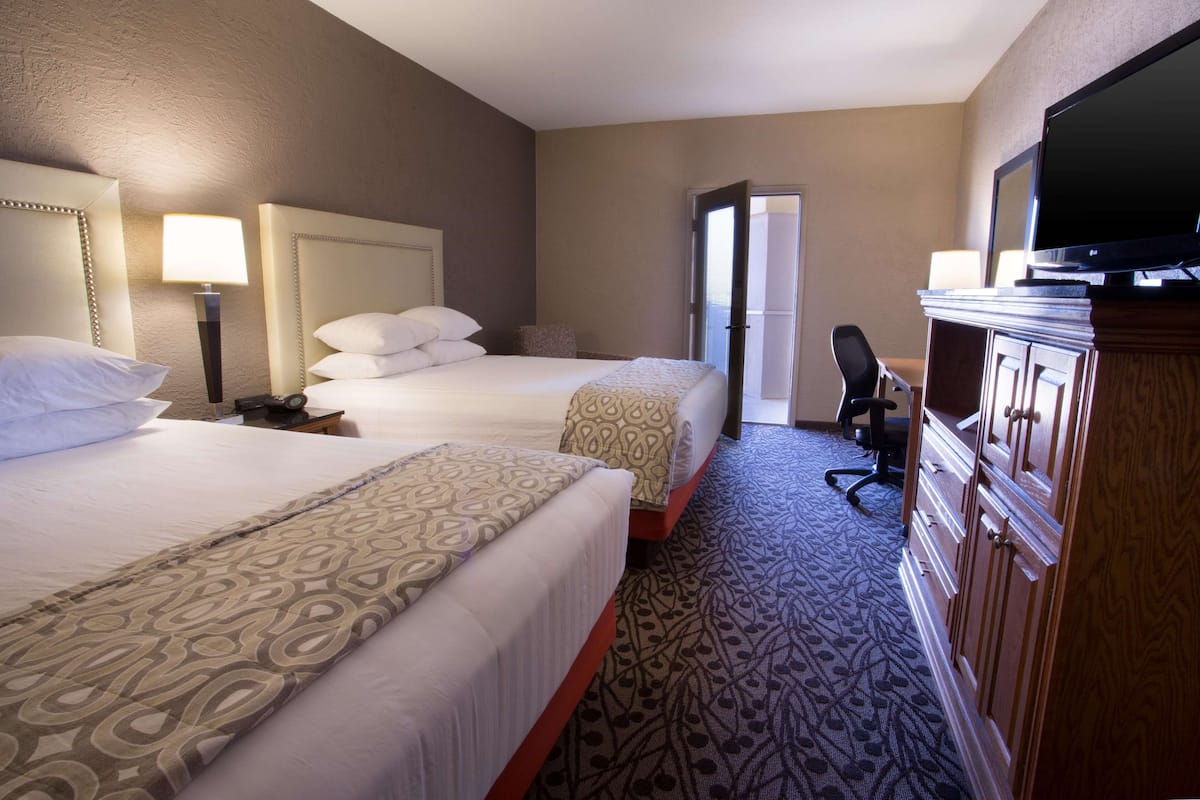 A hotel room with two beds, a television, a desk, and a chair.