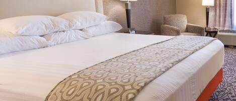 A hotel room with a large bed, two bedside lamps, a chair, and a carpeted floor.