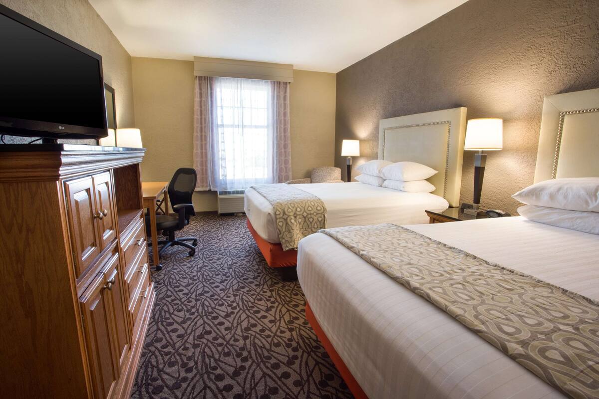 A hotel room with two beds, a desk, a television, and a window with curtains.