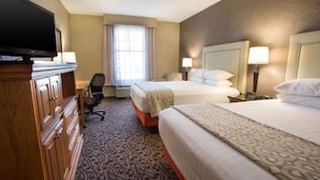 A hotel room with two beds, a desk, a television, and a window with curtains.
