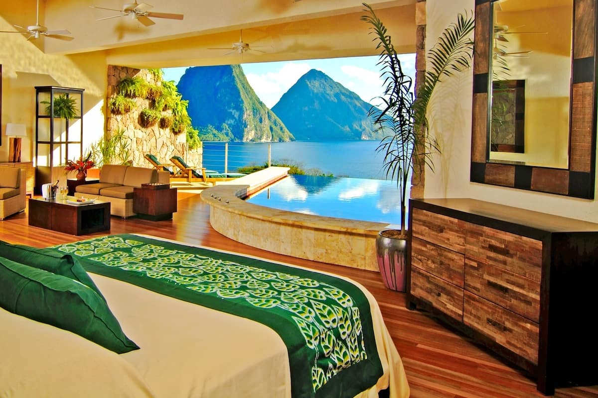 Una habitación amplia con una cama grande, una zona de estar con sofá y sillones, una piscina pequeña y vistas a montañas y agua.