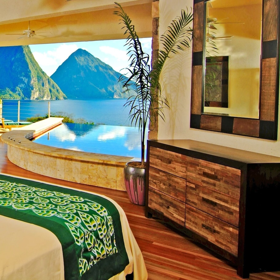A spacious room with a large bed, a seating area with a sofa and armchairs, a small pool, and a view of mountains and water.