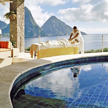 A poolside area with a massage table, lounge chairs, and a view of the sea and mountains.