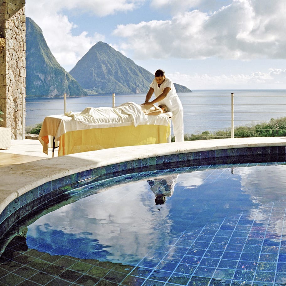 A poolside area with a massage table, lounge chairs, and a view of the sea and mountains.