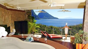 A luxurious bathroom with a large bathtub, a seating area with a view of the ocean, and a balcony with a person standing. - Jade Mountain Resort (Soufrière)