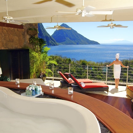 A luxurious bathroom with a large bathtub, a seating area with a view of the ocean, and a balcony with a person standing.