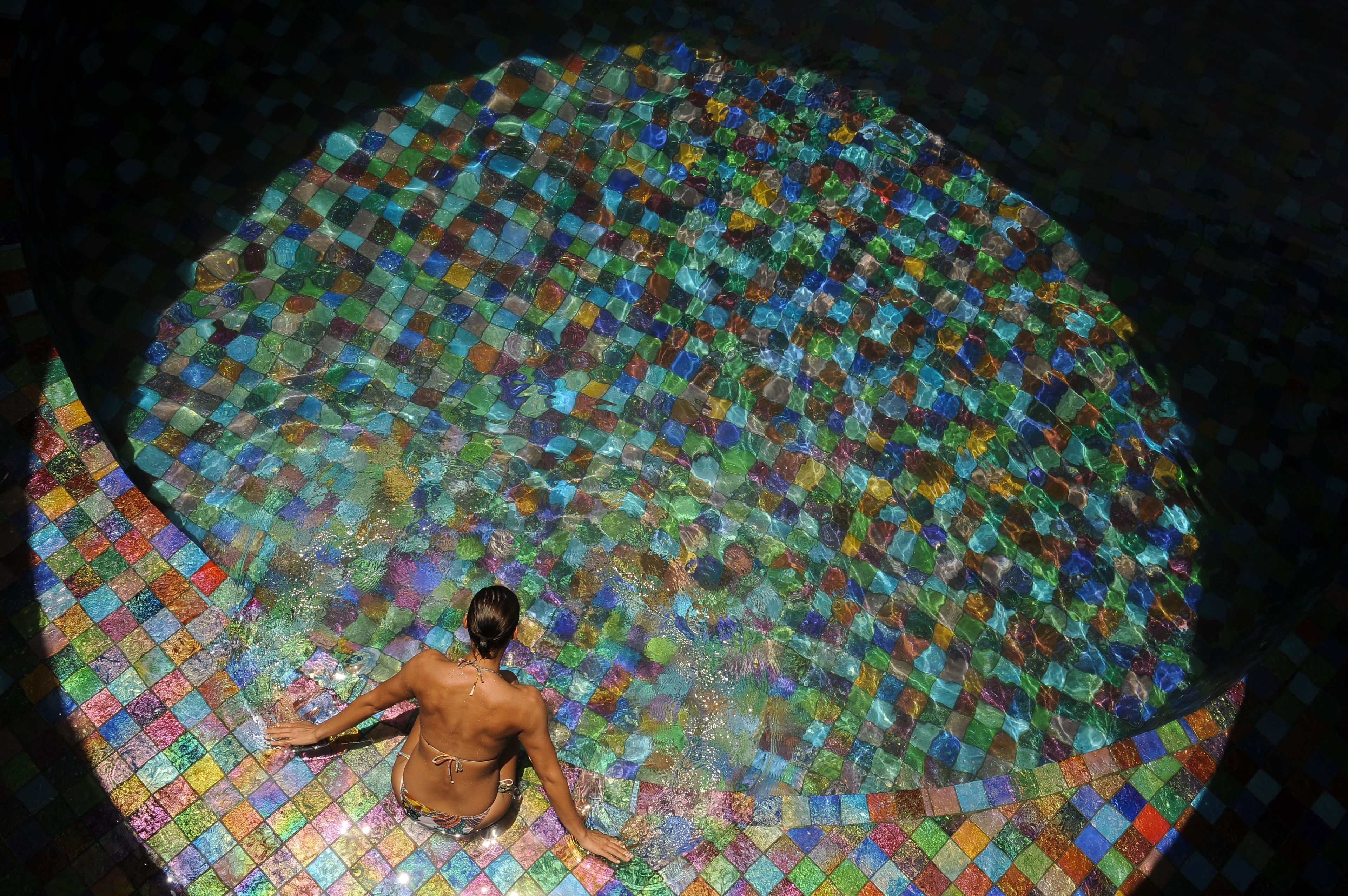 A person sitting in a circular pool with a mosaic tile floor.