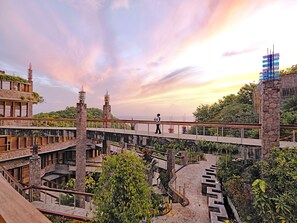 A multi-level hotel with a stone facade, multiple balconies, and a view of the sea at sunset.