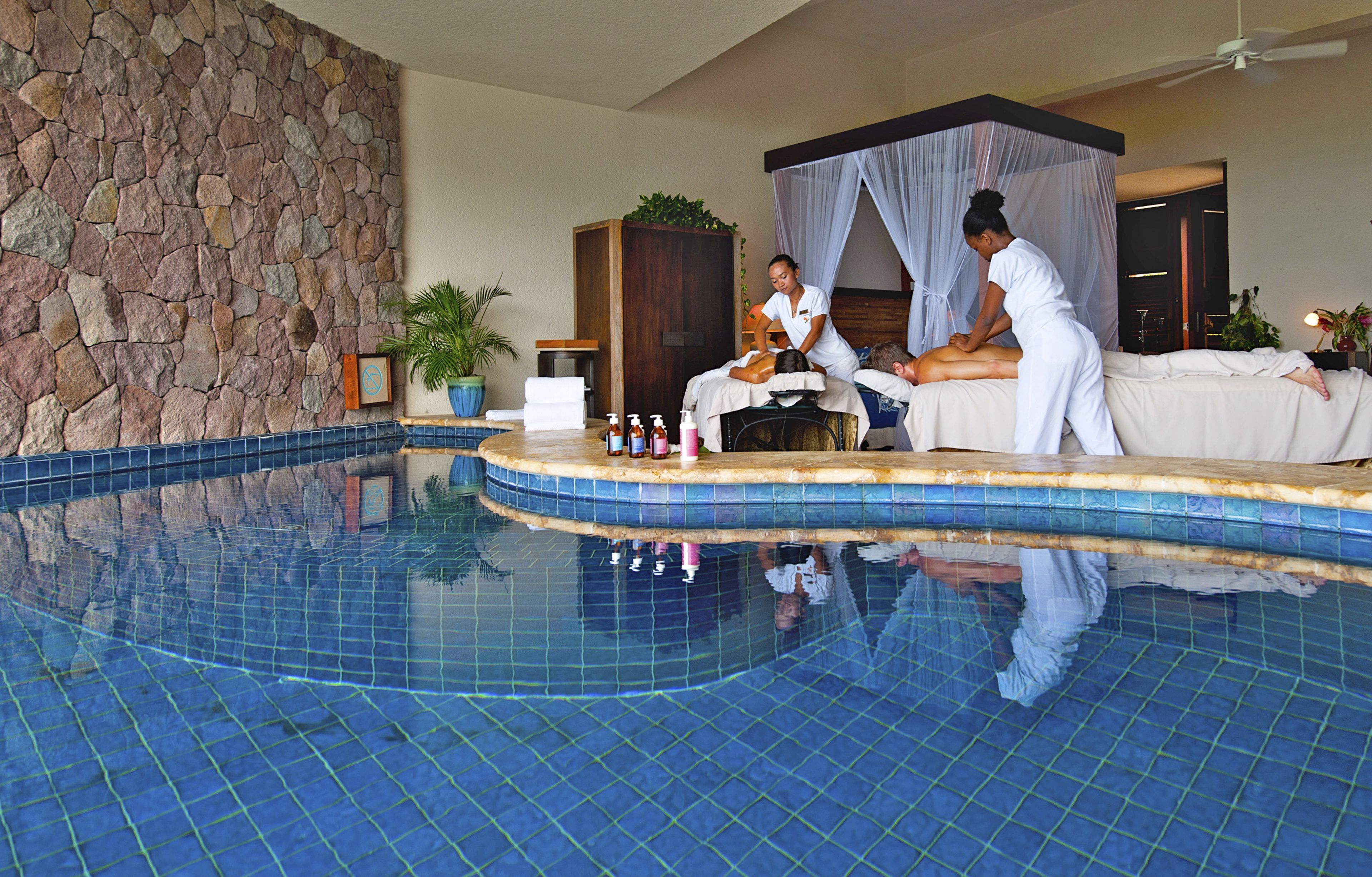 A spa area with a stone wall, a pool, and a massage table.