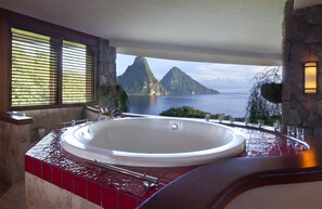A bathroom with a large bathtub, a view of the ocean, and a stone wall.
