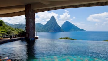 Un puente con mosaicos de colores, una piscina con diseño de cuadros y vistas a una montaña y un cuerpo de agua.