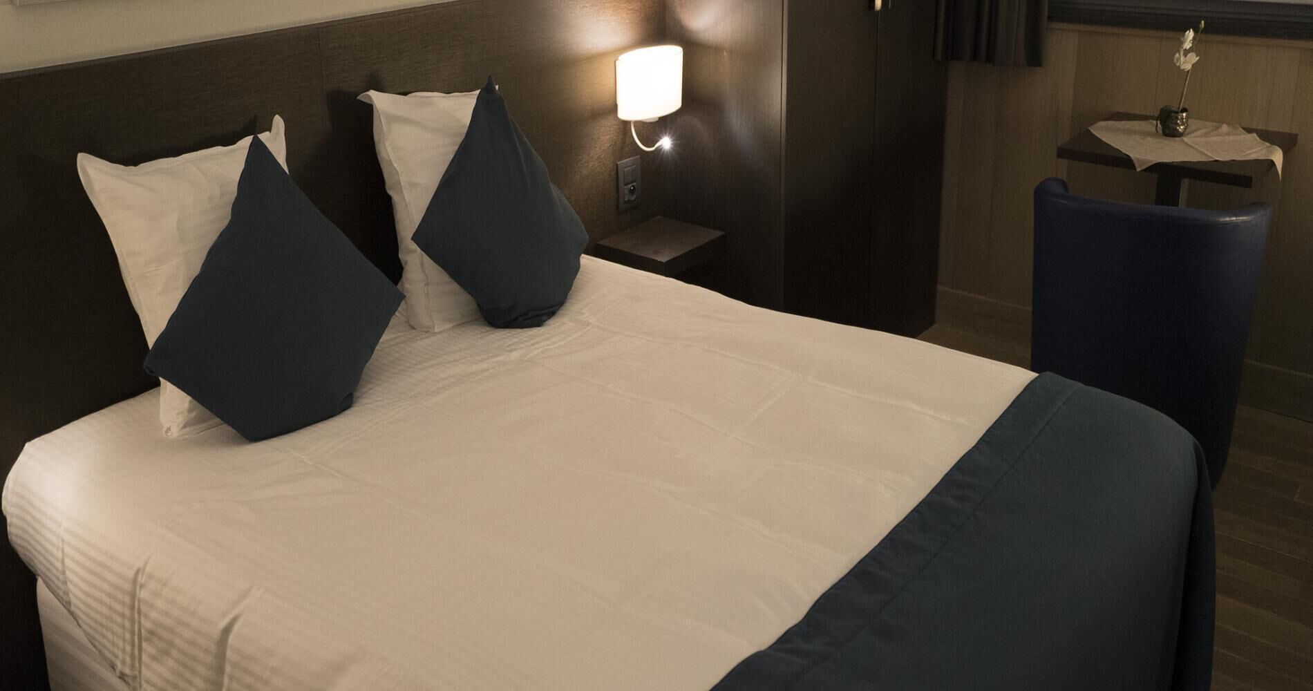 Une chambre d’hôtel avec un lit, des oreillers, une table de chevet, une lampe et une petite table sur laquelle se trouve un vase.