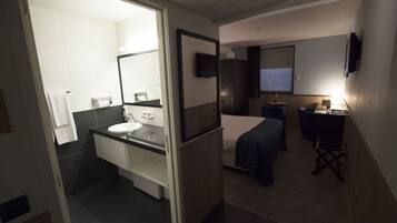 A hotel room with a bathroom, a bed, a desk, and a TV.