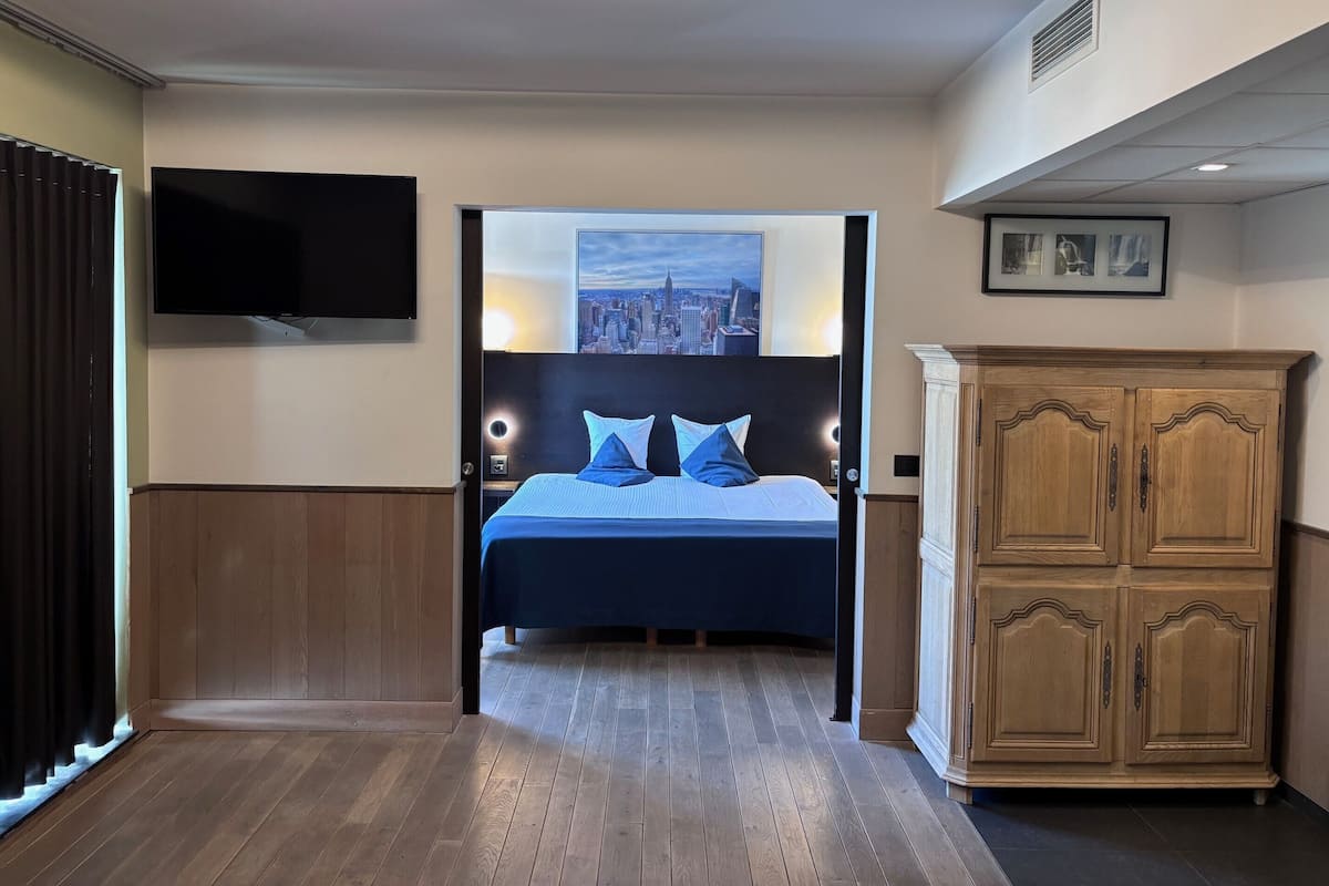 Ein Hotelzimmer mit Bett, Fernseher, Stadtbildgemälde und Holzschrank.
