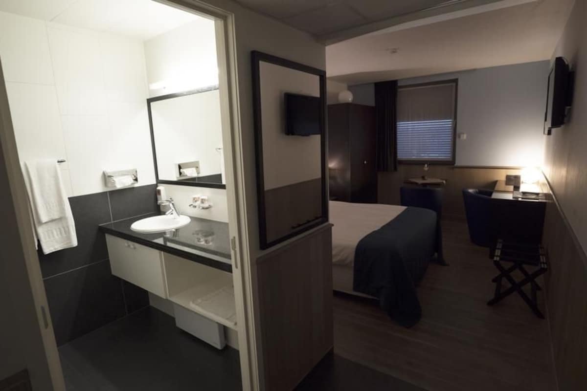 Een kleine hotelkamer met een bed, nachtkastje, televisie en een klein bureau met een lamp.