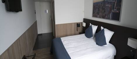 A hotel room with a bed, a TV mounted on the wall, a painting of a cityscape, and a door leading to another room.
