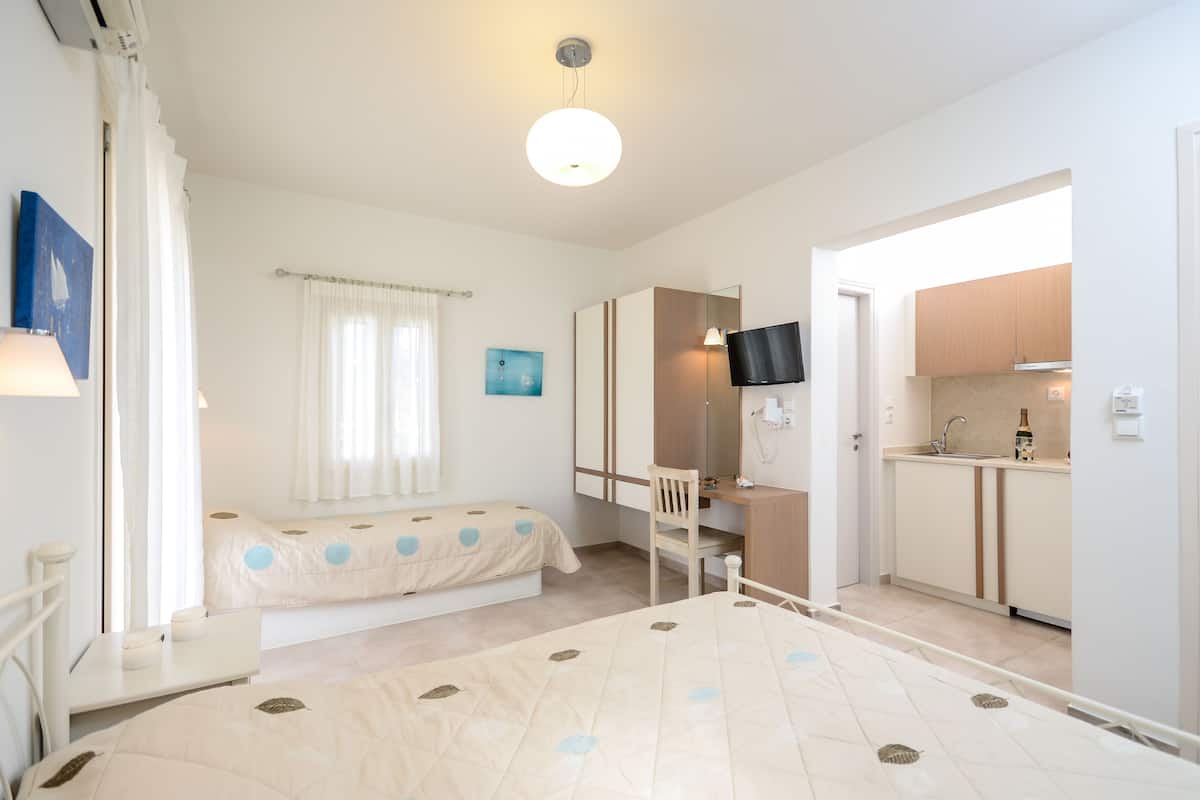 A bedroom with a bed, a bedside table, a chair, a desk, a TV, and a bathroom with a sink and mirror.