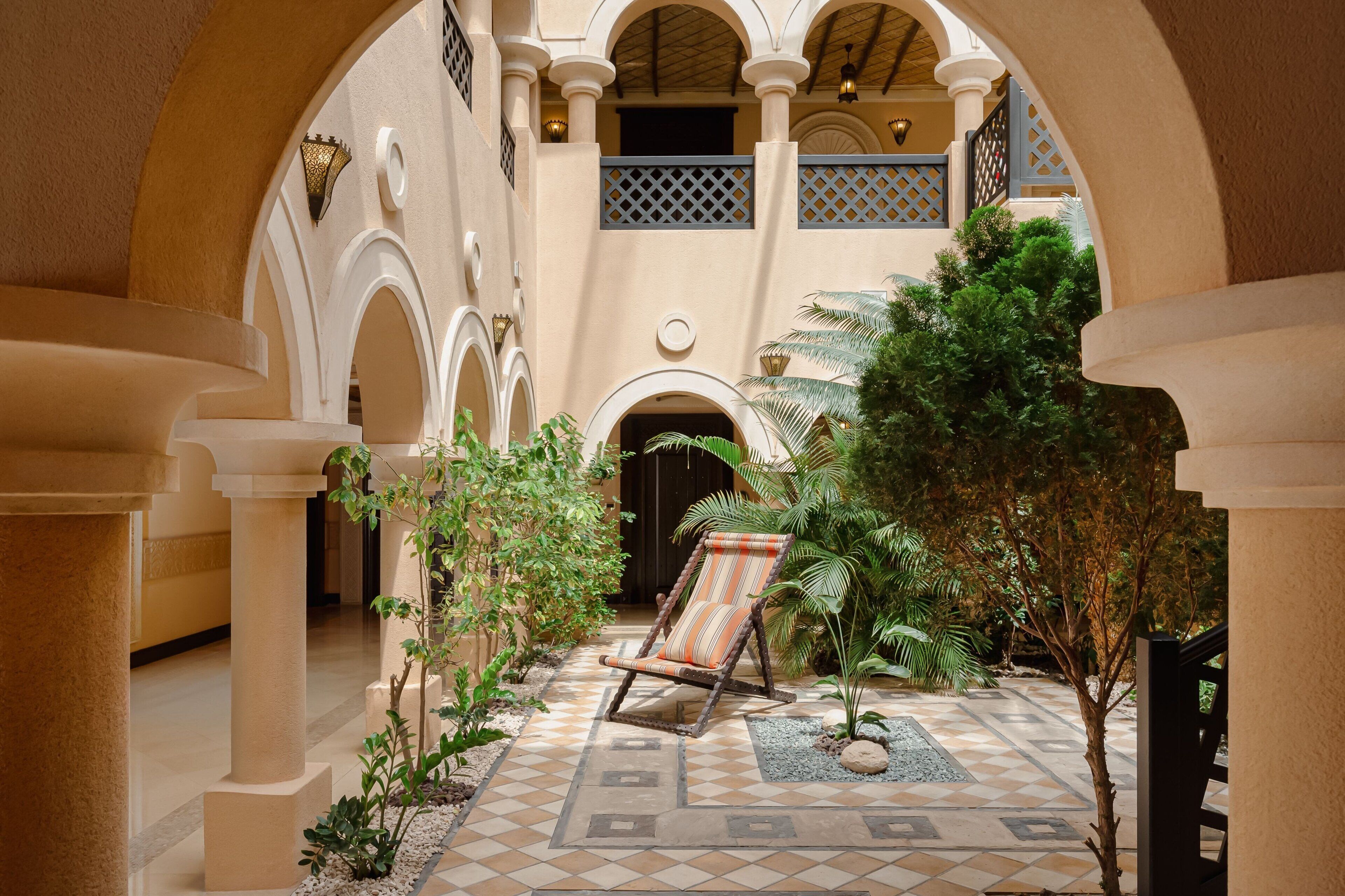 Un patio con una silla de lounge, arcos y suelo de baldosas.