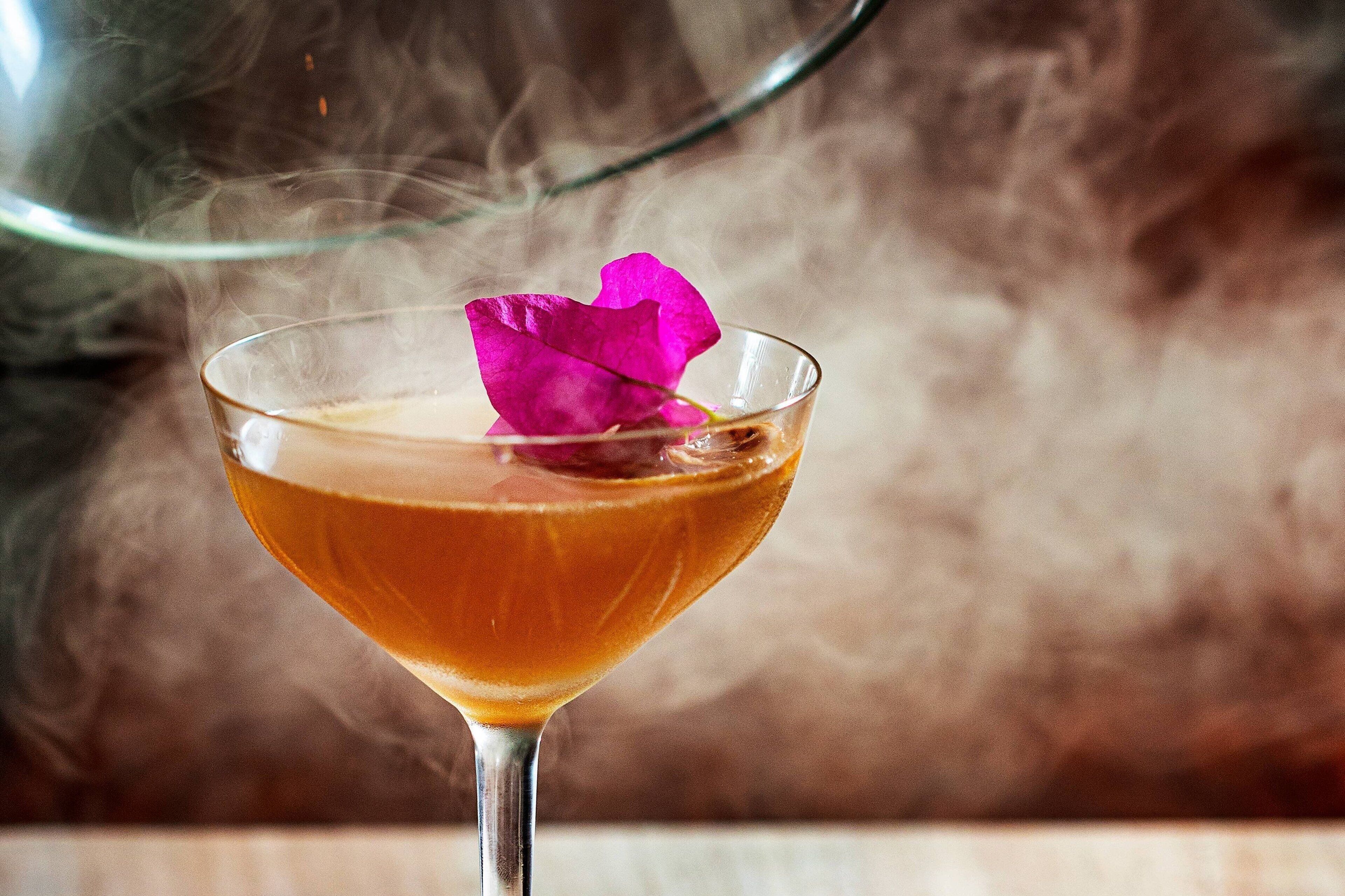 A cocktail with a pink flower garnish in a glass.