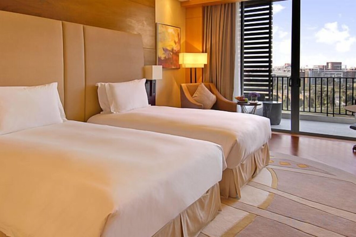 Habitación de hotel con dos camas, un balcón con vistas y una zona de estar con una lámpara.