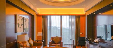 A modern hotel room with a sofa, armchair, and a TV on a cabinet.