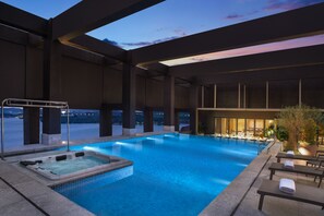A large indoor swimming pool with a hot tub, lounge chairs, and a view of the city at dusk. - Hyatt Regency Dongguan (Dongguan)