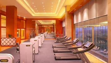 A gym with multiple treadmills and weight machines, a reception desk, and a large window with a view.