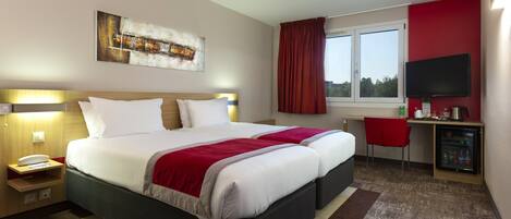 Habitación de hotel con una cama grande, un escritorio con silla, un televisor y un refrigerador pequeño.