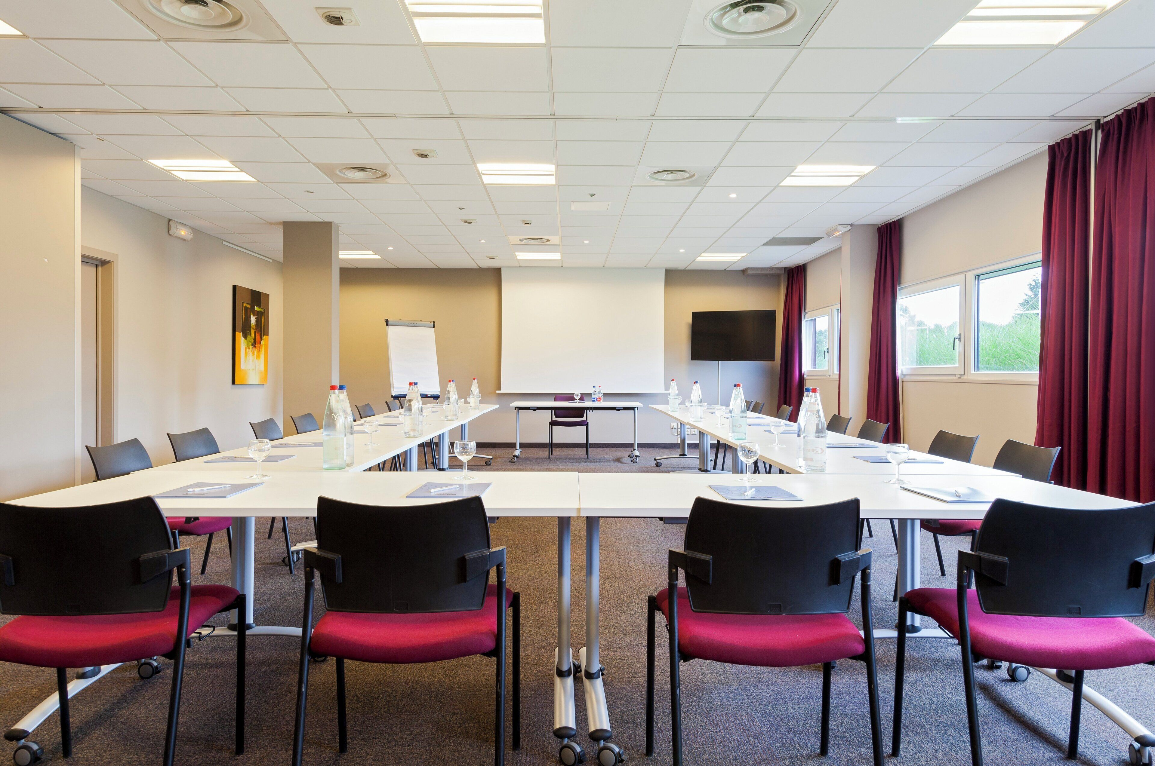 A conference room with a long table, chairs, a projector screen, and a large window with curtains.