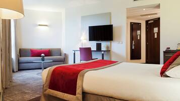 A hotel room with a bed, a sofa, a TV, a desk, and a lamp.